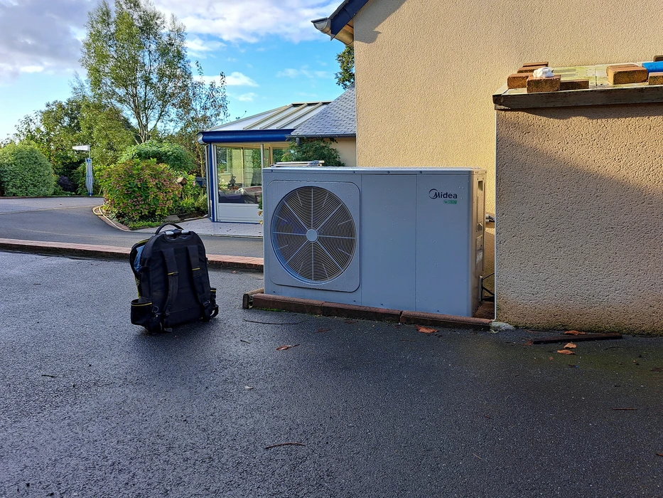 Extérieur d'une maison, pompe à chaleur air-eau **Midea** installée contre un mur en crépi, posée sur un socle
