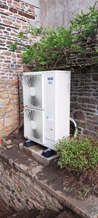 Unité extérieure de pompe à chaleur air/eau installée en extérieur, contre un mur en pierre, sur plots anti-vibratoires