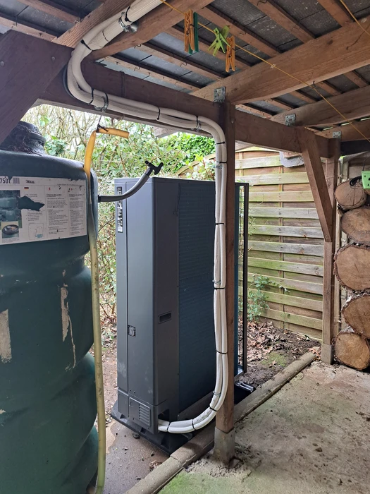 Installation extérieure d'une pompe à chaleur air/eau verticale de couleur anthracite, positionnée sous un auvent en bois