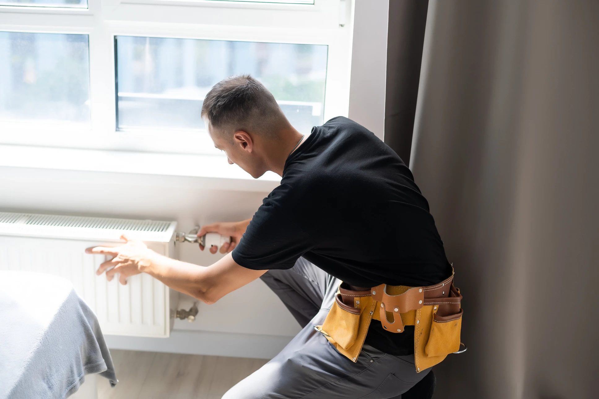 Homme travaillant sur un radiateur près d'une fenêtre dans un intérieur résidentiel moderne