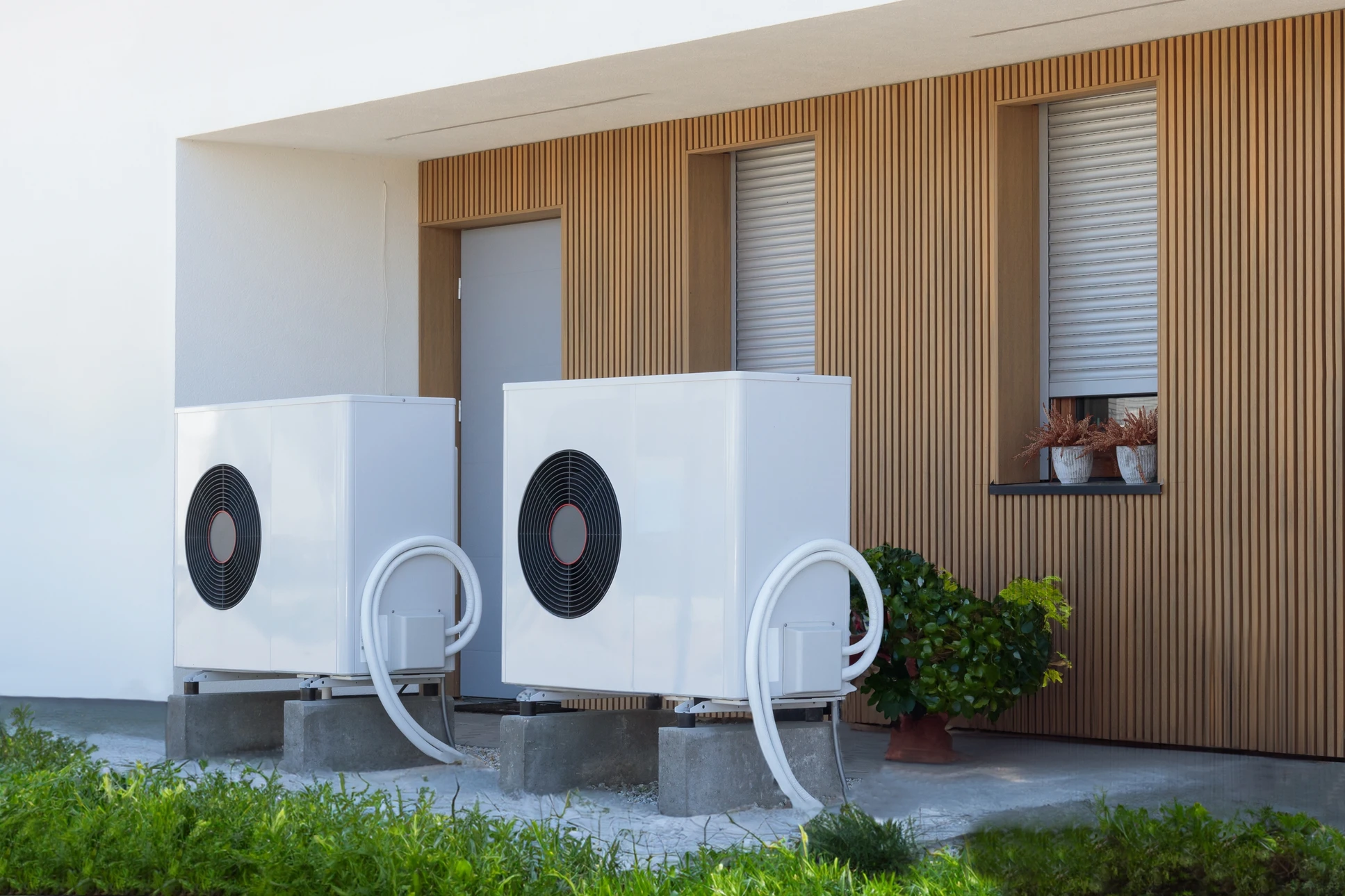 Extérieur résidentiel moderne avec deux unités de pompe à chaleur air-eau installées sur socles béton