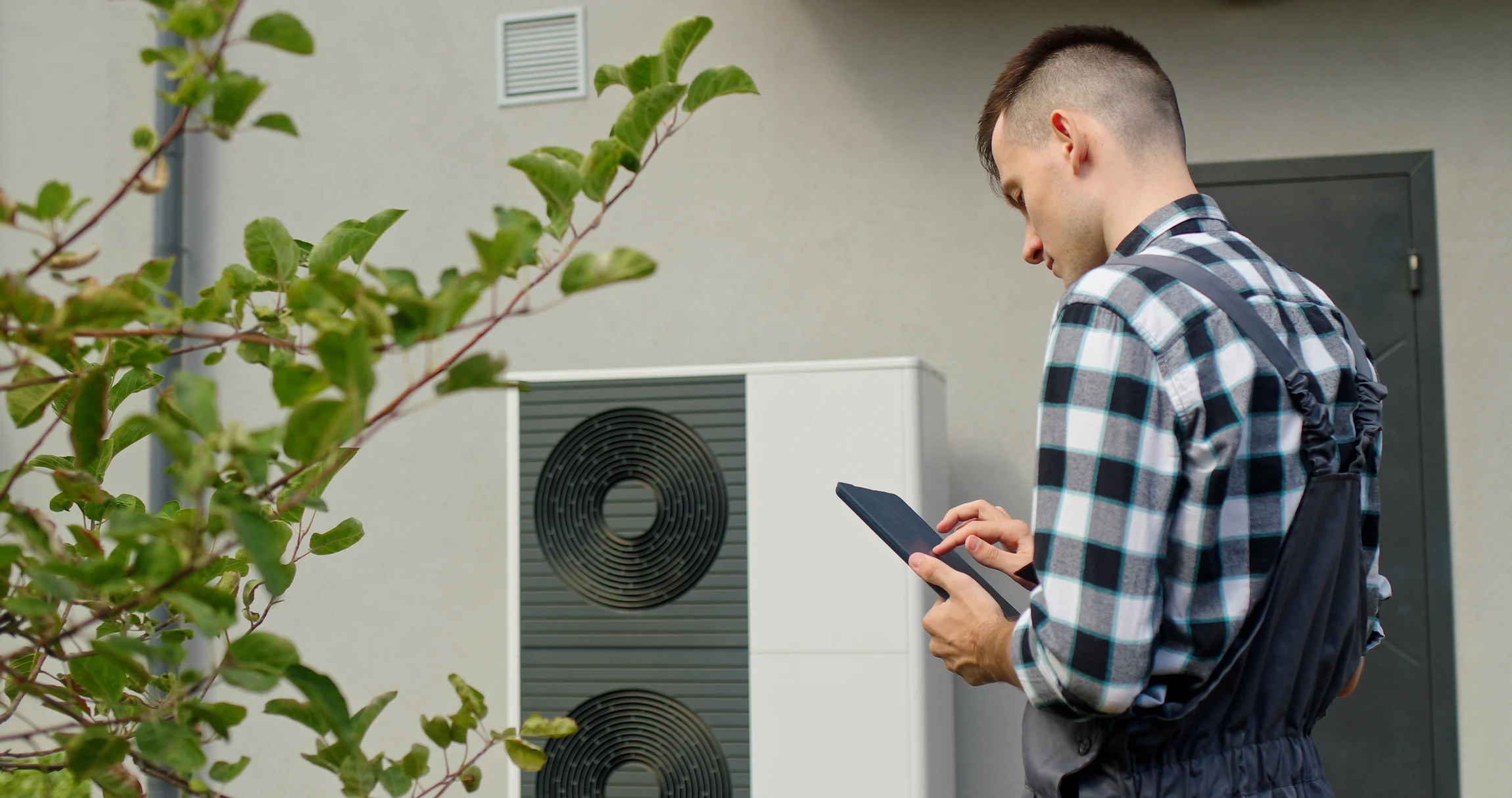 Un technicien utilise une tablette pour régler les Paramètres d'une pompe à chaleur externe à l'extérieur d'une maison