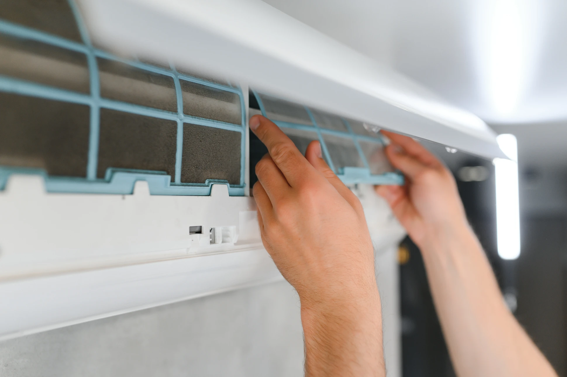 Un technicien en uniforme bleu et casquette noire installe ou remplace un filtre à air dans un système de ventilation plafond intérieur blanc