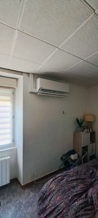 Chambre résidentielle avec climatiseur mural split system monté en hauteur sur mur gris, unité intérieure type monosplit
