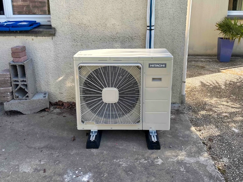 Unité extérieure de climatisation/pompe à chaleur Hitachi, installée en extérieur sur plots anti-vibratoires, posée sur dallage béton contre un mur crépi