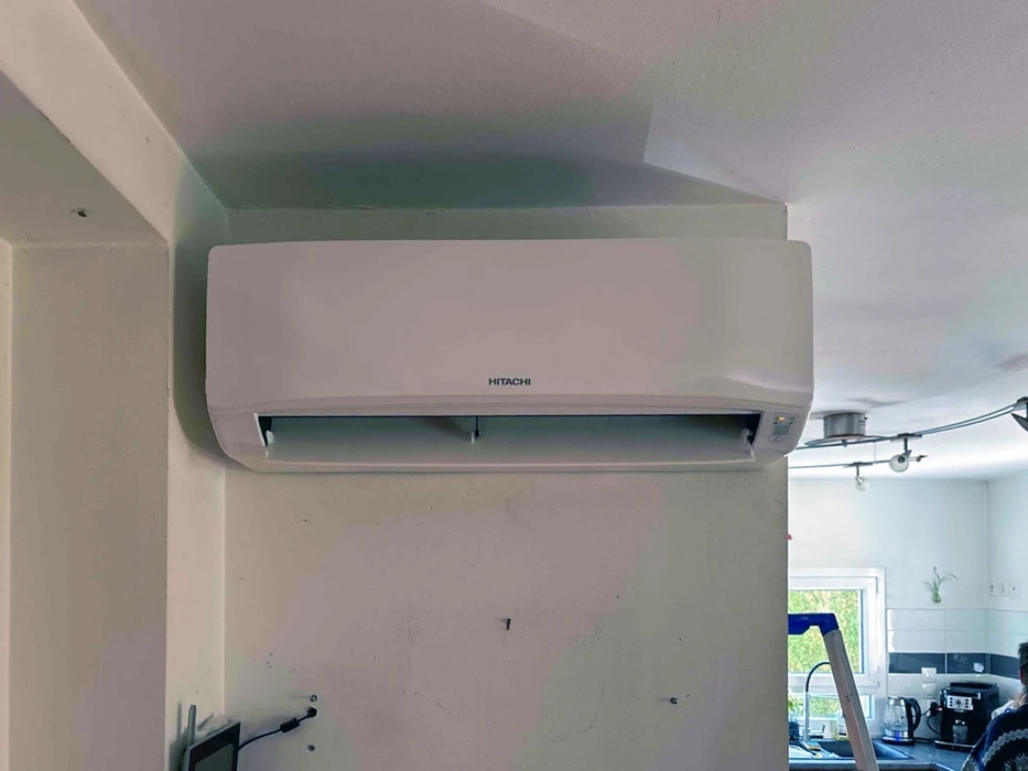Intérieur résidentiel, mur blanc, unité intérieure de climatisation murale split système marque **Hitachi**, coloris blanc cassé, montée en hauteur près du plafond