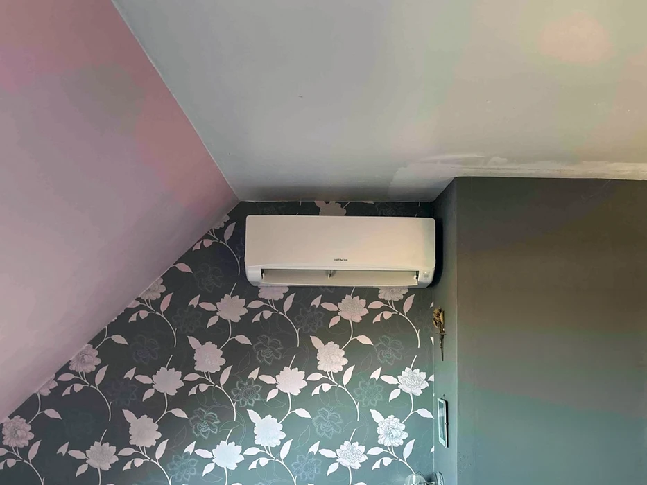 Unité intérieure de climatisation murale **Hitachi** installée en hauteur dans une pièce d'habitation