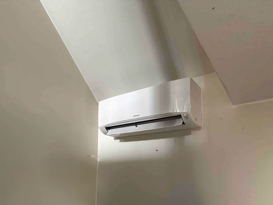 Unité intérieure de climatisation split murale Hitachi, blanc brillant, fixée en hauteur dans un angle de pièce aux murs beiges
