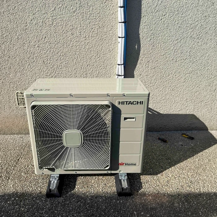 Unité extérieure de climatisation **Hitachi airHome** installée contre un mur extérieur en béton