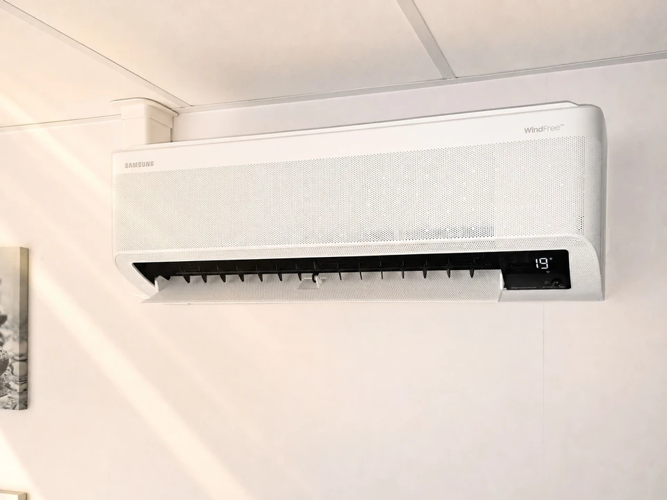 Un technicien en uniforme bleu et casquette noire installe ou remplace un filtre à air dans un système de ventilation plafond intérieur blanc